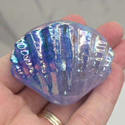 Hand holding a blue and purple iridescent crystal clam carving against a neutral background