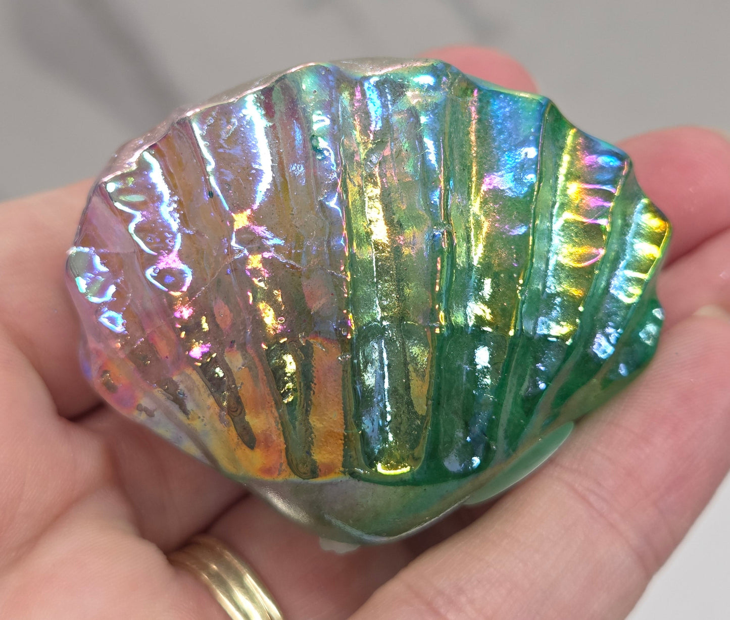 Hand holding a pink and green iridescent crystal clam carving against a neutral background