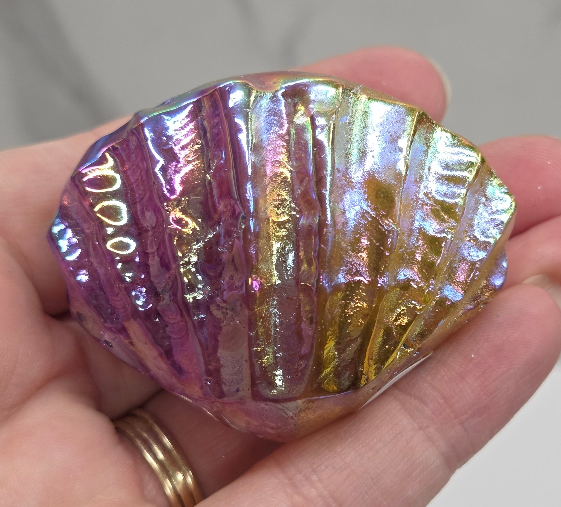 Hand holding a purple and yellow  iridescent crystal clam carving against a neutral background