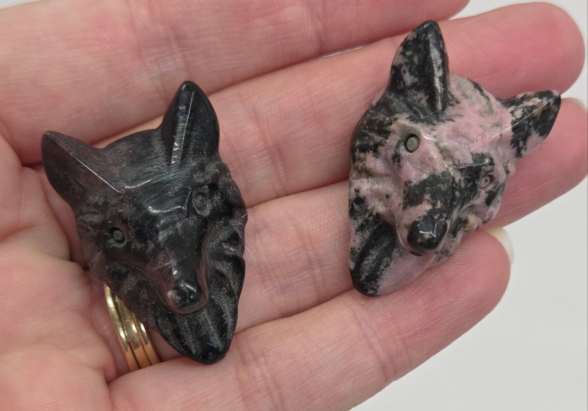 Two wolf head crystal carvings in a variety of materials held in a hand against a plain background