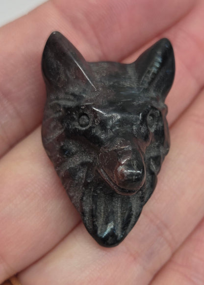 Person holding a black and red Garnet carving shaped like a wolf  face 