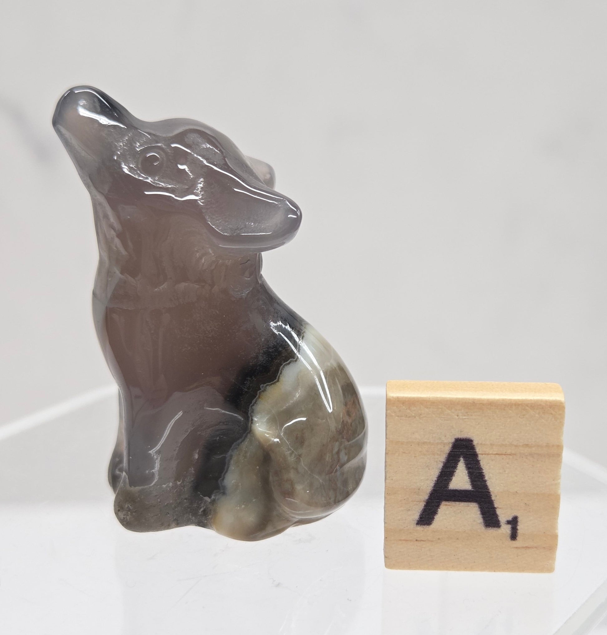 Volcano Agate wolf carving on a clear stand, next to a wooden block with 'A' on a white background