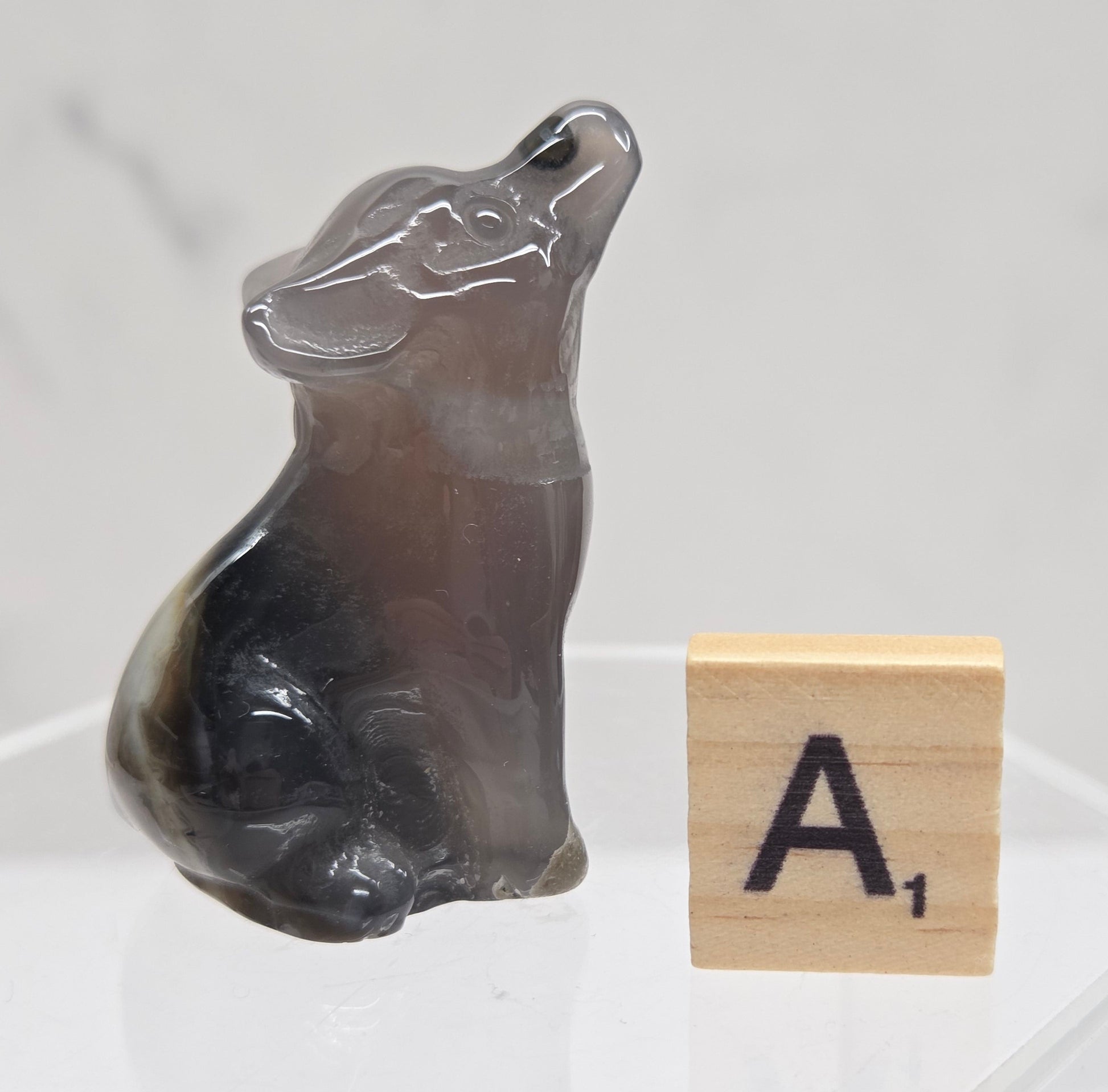 Volcano Agate wolf carving on a clear stand, next to a wooden block with 'A' on a white background