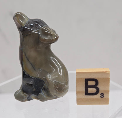 Volcano Agate wolf carving on a clear stand, next to a wooden block with 'B' on a white background