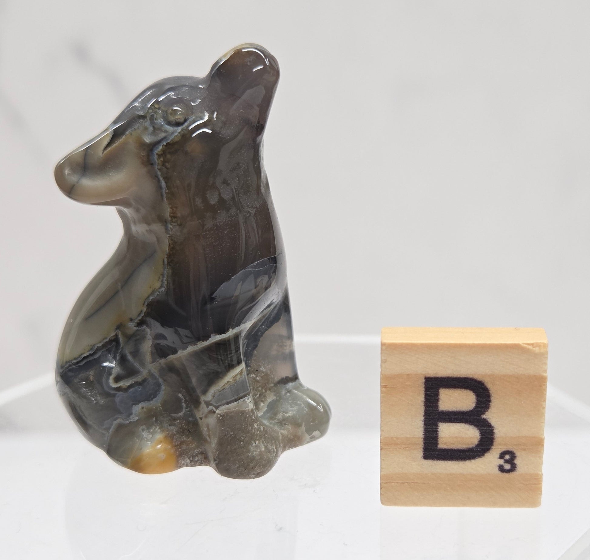 Volcano Agate wolf carving on a clear stand, next to a wooden block with 'B' on a white background