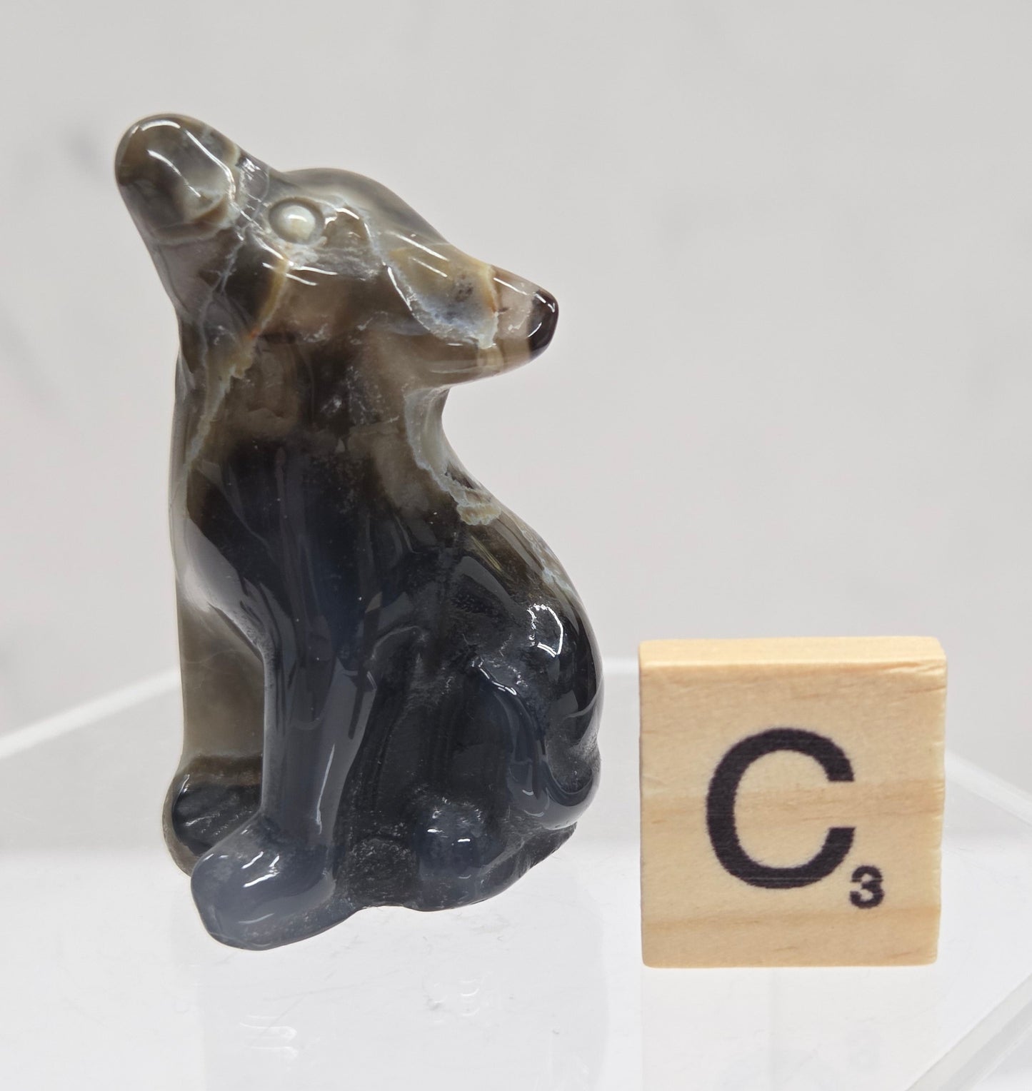 Volcano Agate wolf carving on a clear stand, next to a wooden block with 'C' on a white background
