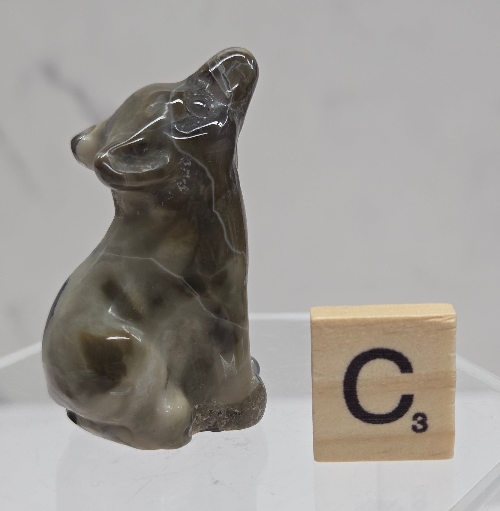 Volcano Agate wolf carving on a clear stand, next to a wooden block with 'C' on a white background