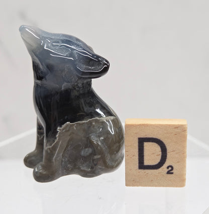 Volcano Agate wolf carving on a clear stand, next to a wooden block with 'D' on a white background