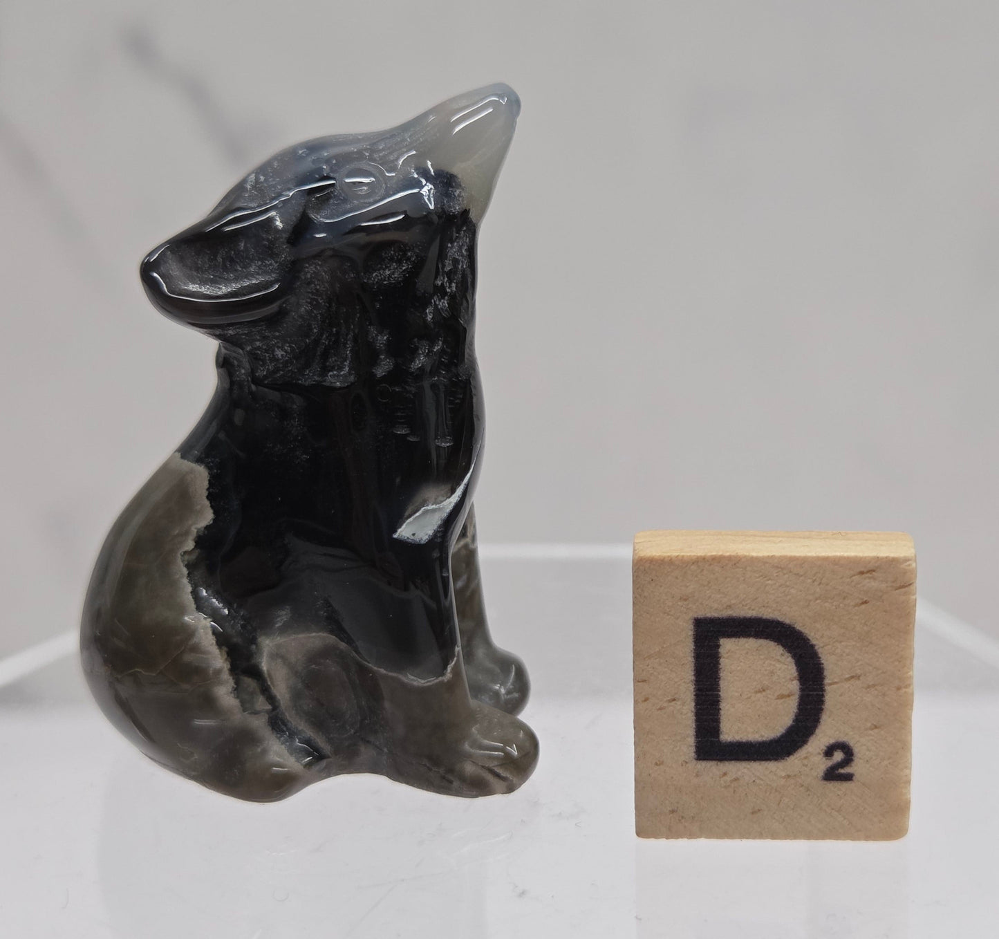 Volcano Agate wolf carving on a clear stand, next to a wooden block with 'D' on a white background