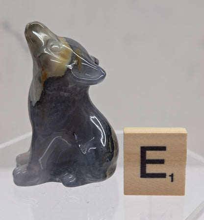 Volcano Agate wolf carving on a clear stand, next to a wooden block with 'E' on a white background
