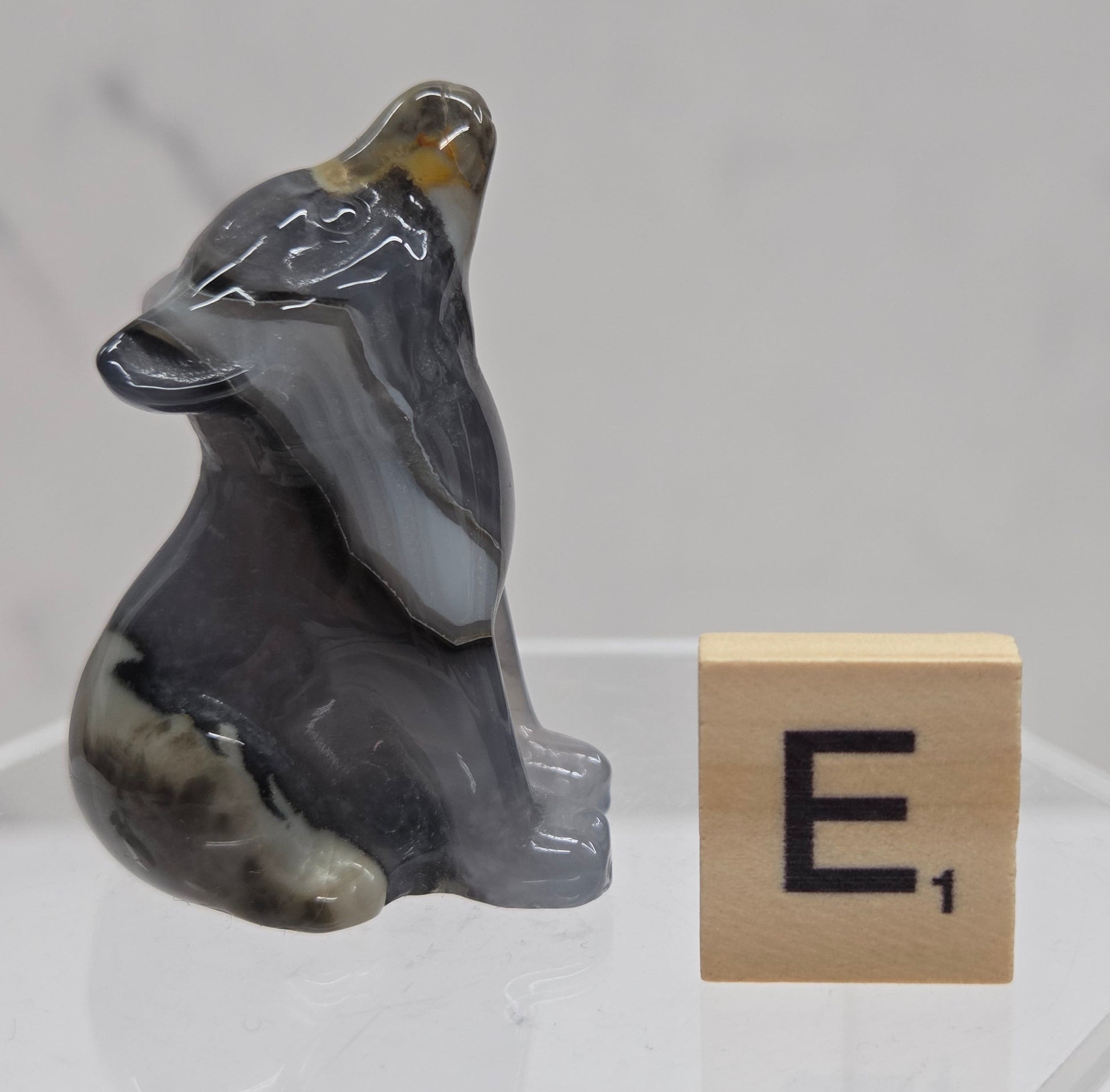 Volcano Agate wolf carving on a clear stand, next to a wooden block with 'E' on a white background