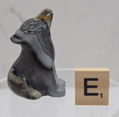 Volcano Agate wolf carving on a clear stand, next to a wooden block with 'E' on a white background