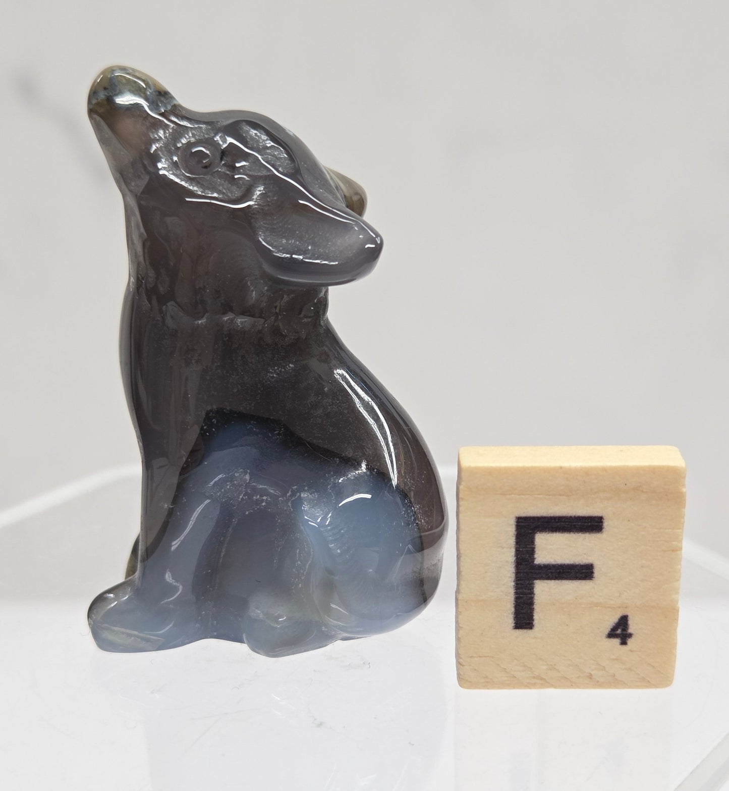 Volcano Agate wolf carving on a clear stand, next to a wooden block with 'F' on a white background