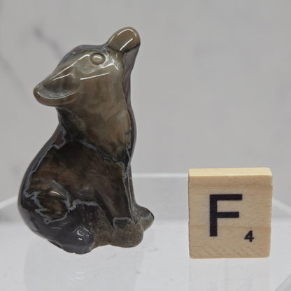 Volcano Agate wolf carving on a clear stand, next to a wooden block with 'F' on a white background