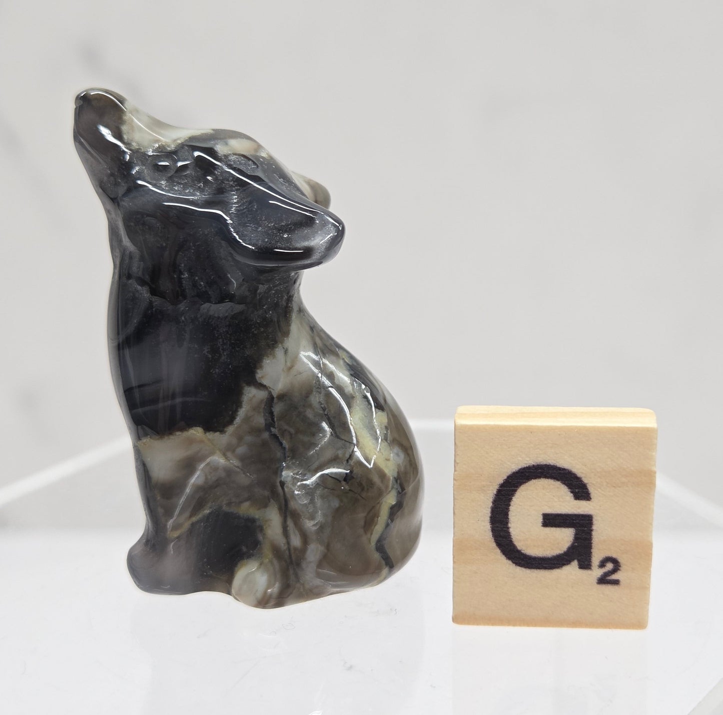 Volcano Agate wolf carving on a clear stand, next to a wooden block with 'G' on a white background