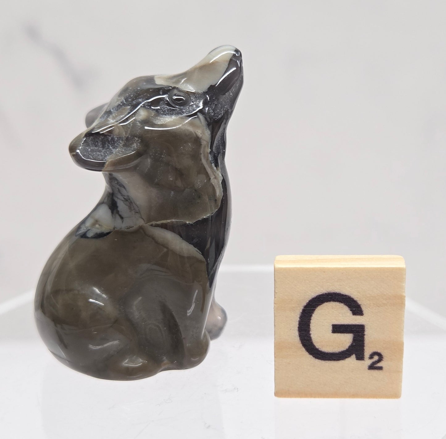Volcano Agate wolf carving on a clear stand, next to a wooden block with 'G' on a white background