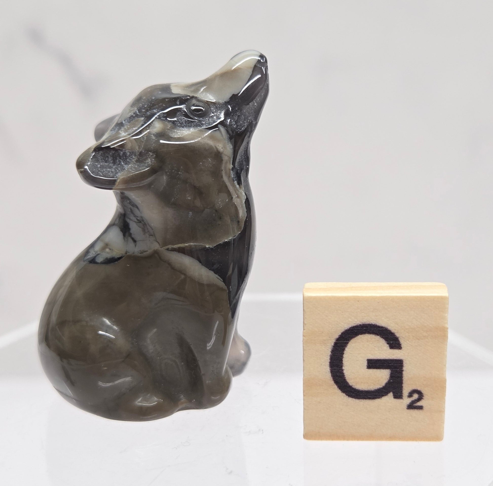 Volcano Agate wolf carving on a clear stand, next to a wooden block with 'G' on a white background