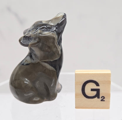 Volcano Agate wolf carving on a clear stand, next to a wooden block with 'G' on a white background