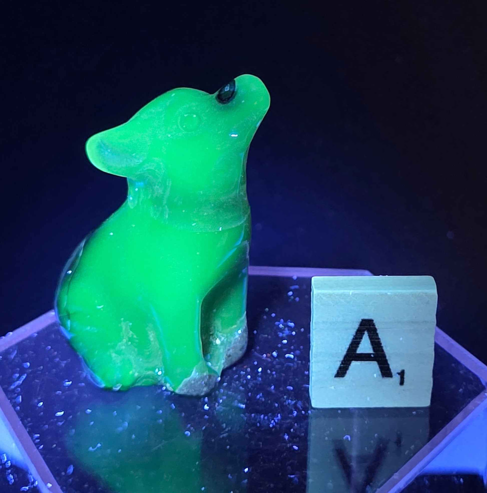 Volcano Agate wolf carving on a clear stand, next to a wooden block with 'A' under UV light