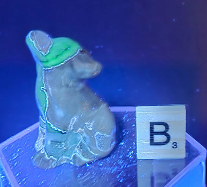 Volcano Agate wolf carving on a clear stand, next to a wooden block with 'B' under UV light