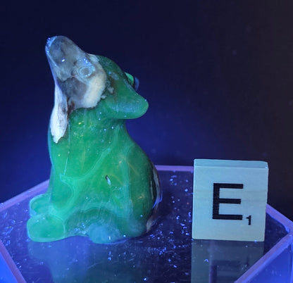 Volcano Agate wolf carving on a clear stand, next to a wooden block with 'E' under UV light
