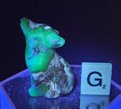 Volcano Agate wolf carving on a clear stand, next to a wooden block with 'G' under UV light