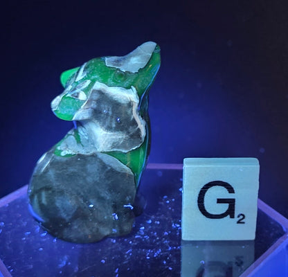Volcano Agate wolf carving on a clear stand, next to a wooden block with 'G' under UV light