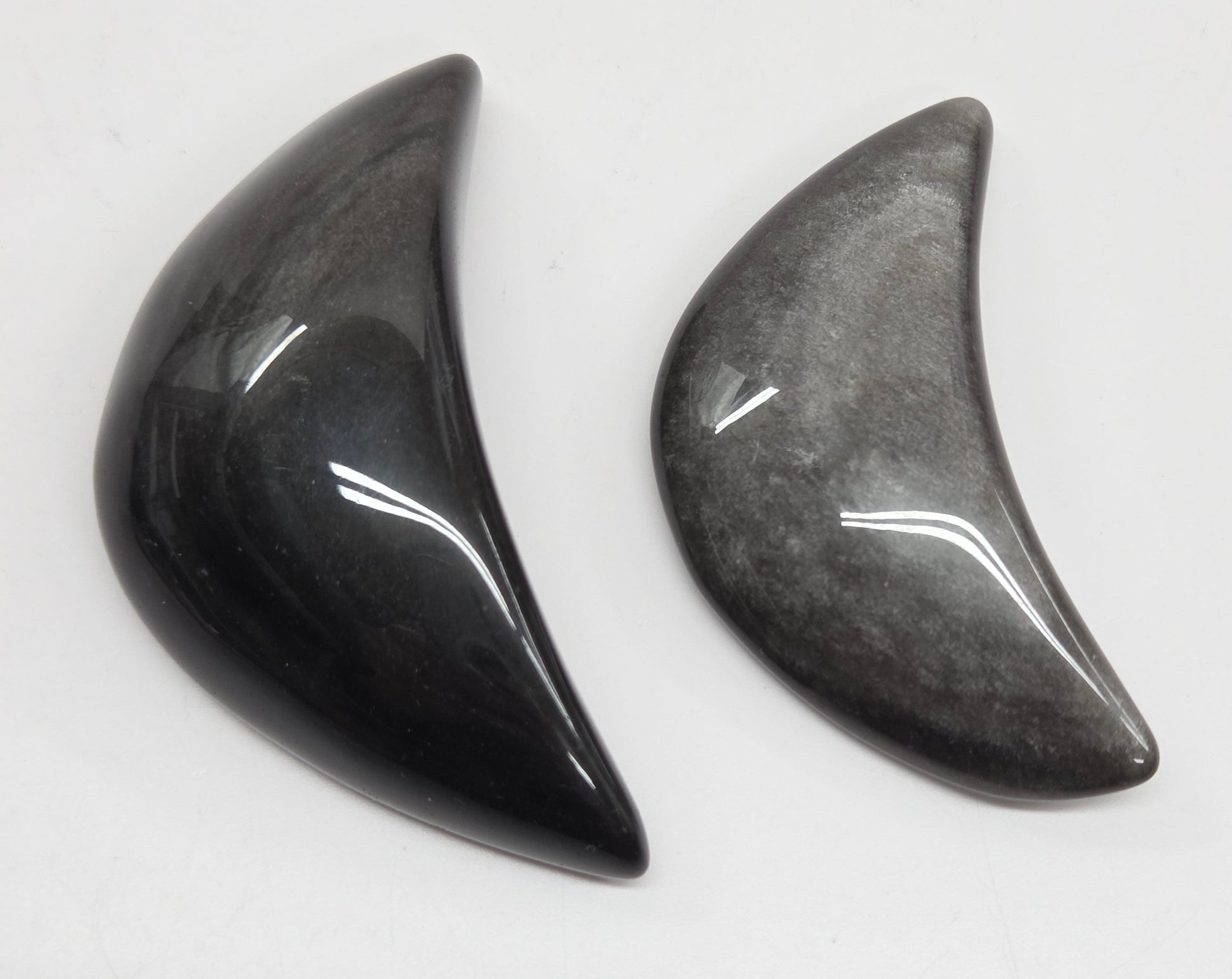 Two silver sheen obsidian crescent moon carvings on a white background