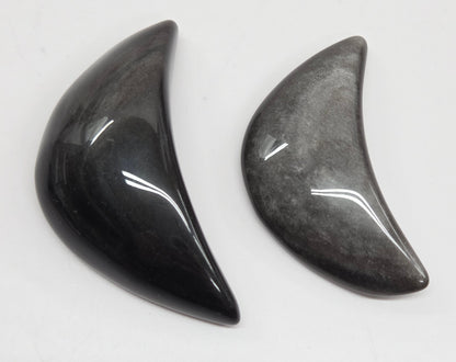 Two silver sheen obsidian crescent moon carvings on a white background