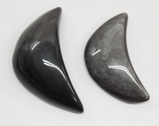 Two silver sheen obsidian crescent moon carvings on a white background