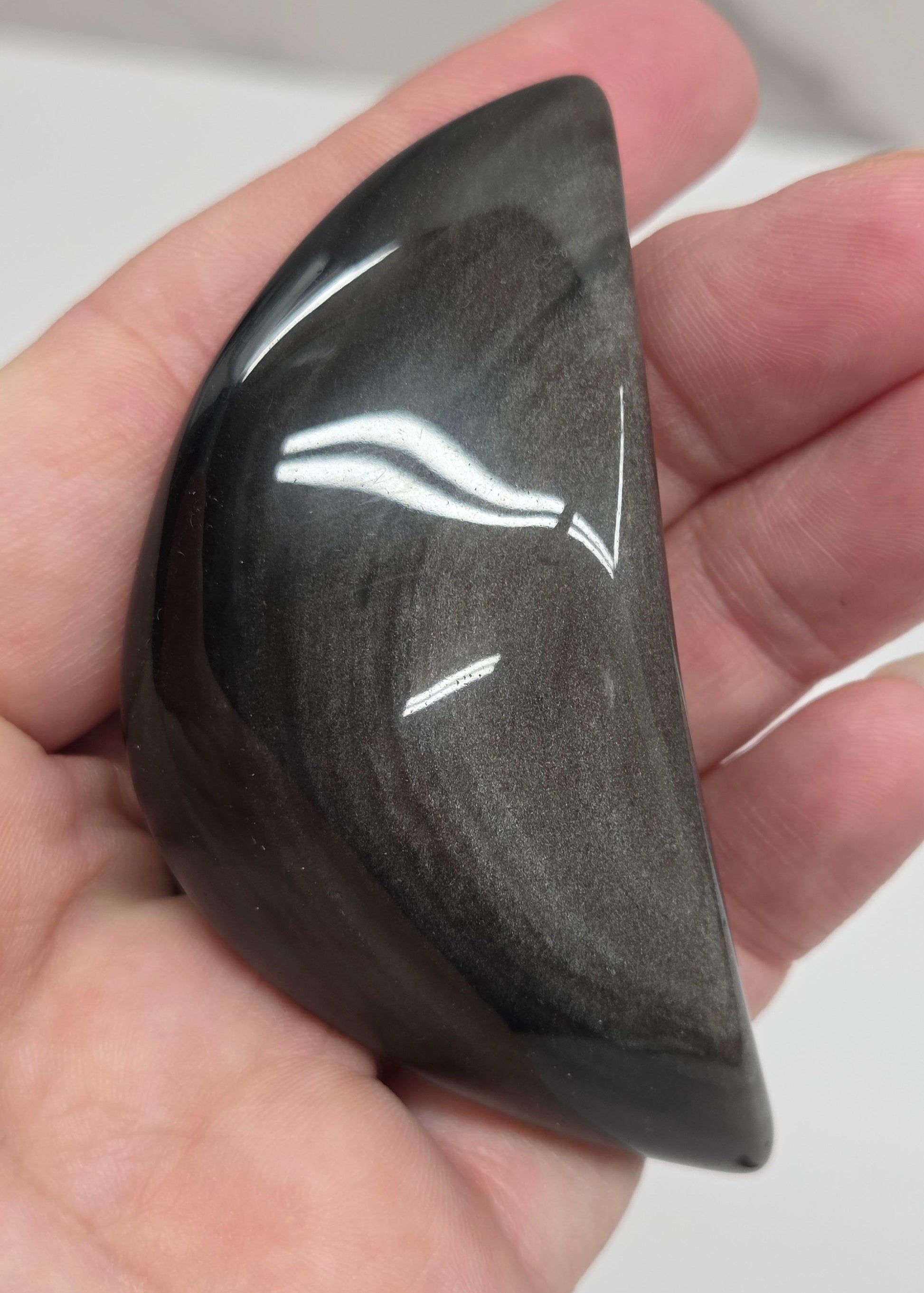 Hand holding a silver sheen obsidian crescent moon carving on a white background