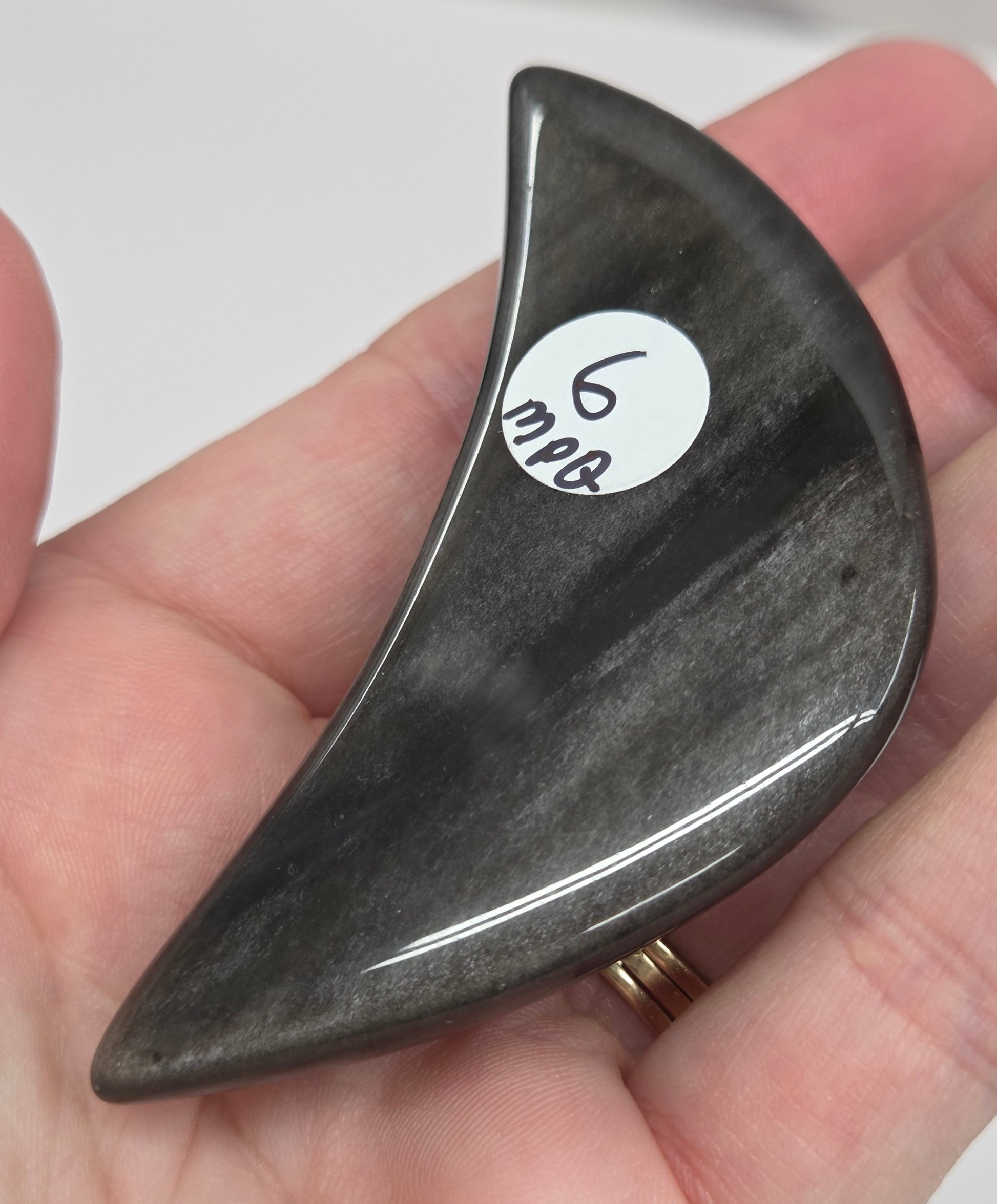 Hand holding a silver sheen obsidian crescent moon carving on a white background