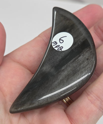 Hand holding a silver sheen obsidian crescent moon carving on a white background