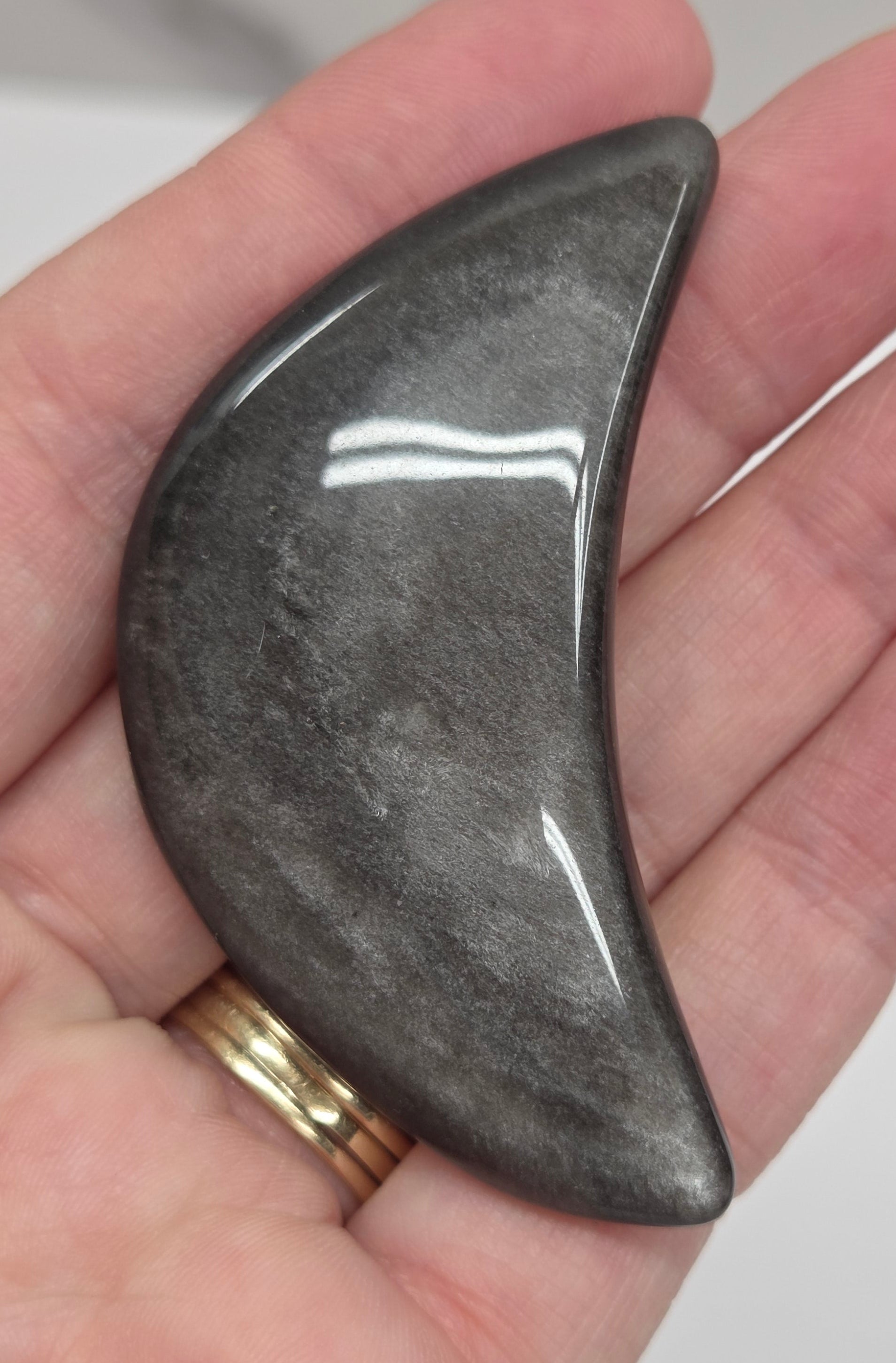 Hand holding a silver sheen obsidian crescent moon carving on a white background