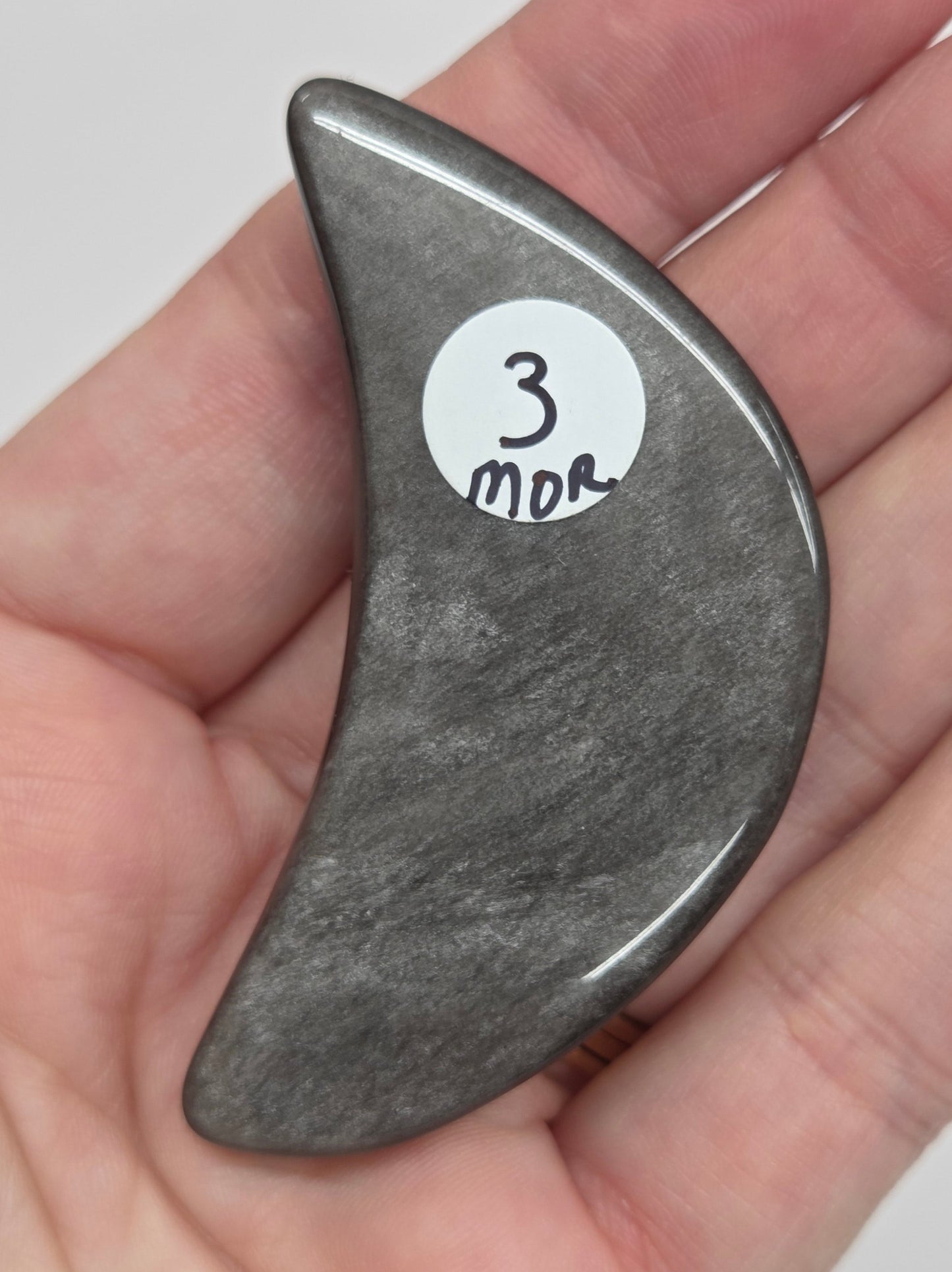 Hand holding a silver sheen obsidian crescent moon carving on a white background