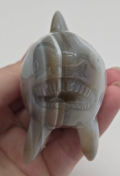 Hand holding an Agate shark carving with banding on a white background