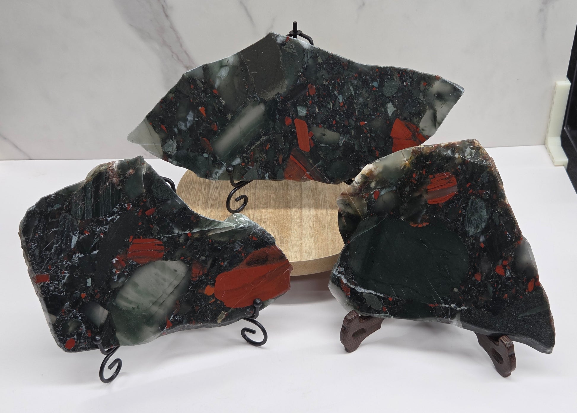 Three dark stone African Bloodstone slabs with red and gray patterns on a white surface.