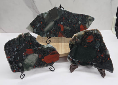 Three dark stone African Bloodstone slabs with red and gray patterns on a white surface.