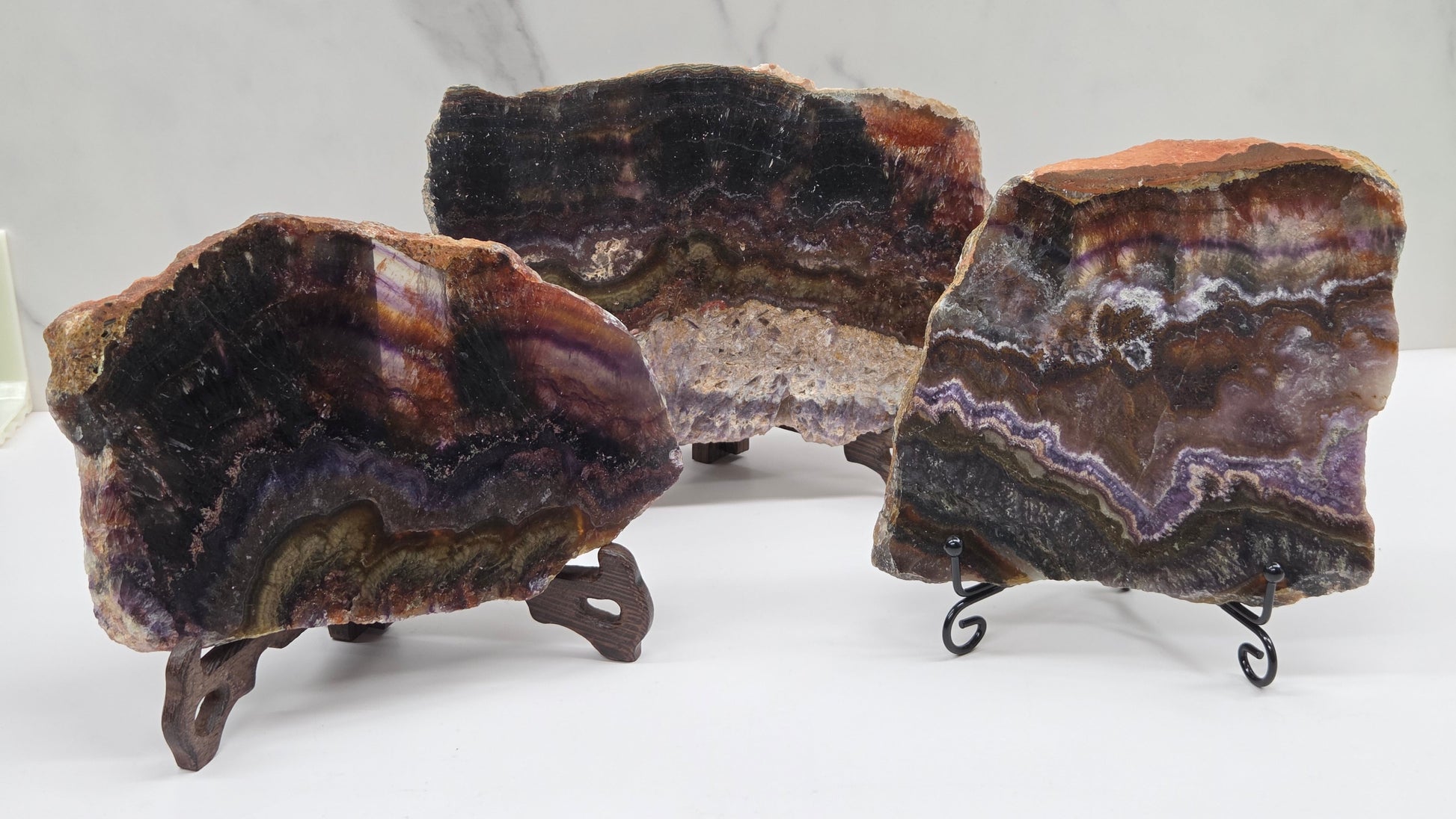 Three banded crystal slices with multiple colors and inclusions on stands against a marble background