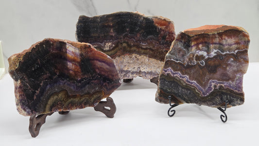 Three banded crystal slices with multiple colors and inclusions on stands against a marble background