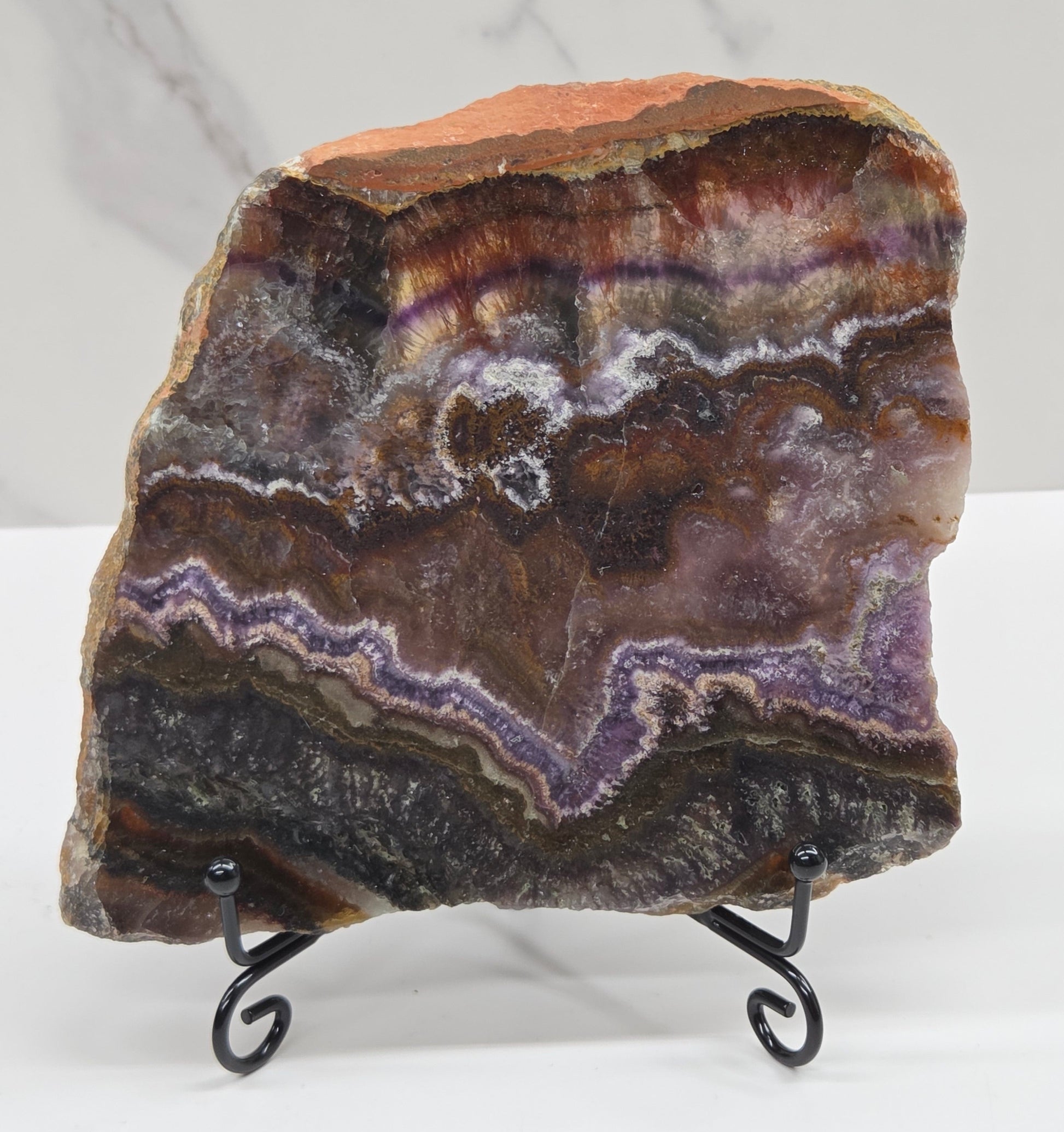 Banded crystal slice with multiple colors and inclusions on a stand against a marble background
