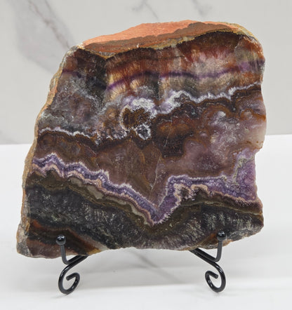 Banded crystal slice with multiple colors and inclusions on a stand against a marble background