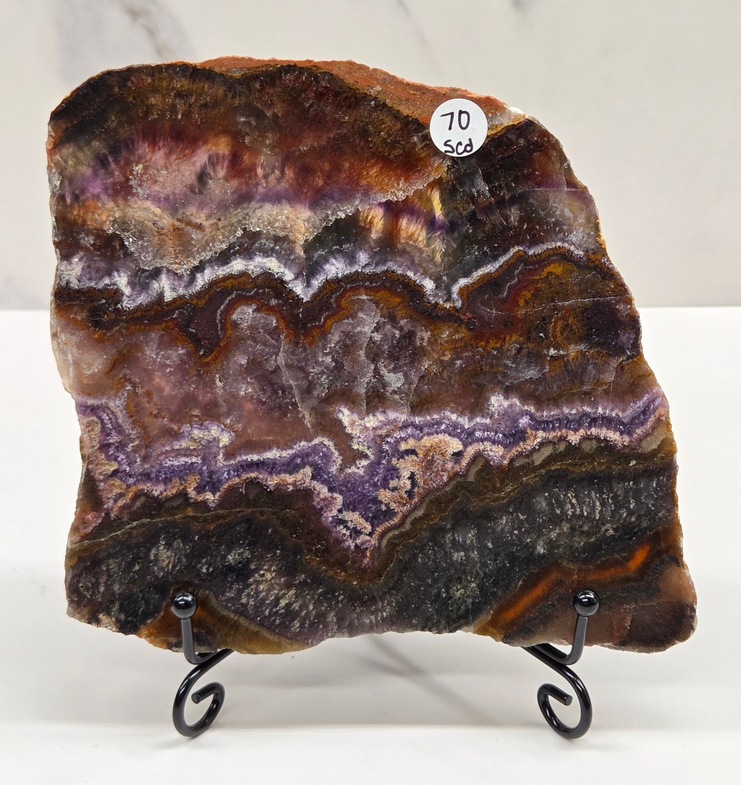 Banded crystal slice with multiple colors and inclusions on a stand against a marble background