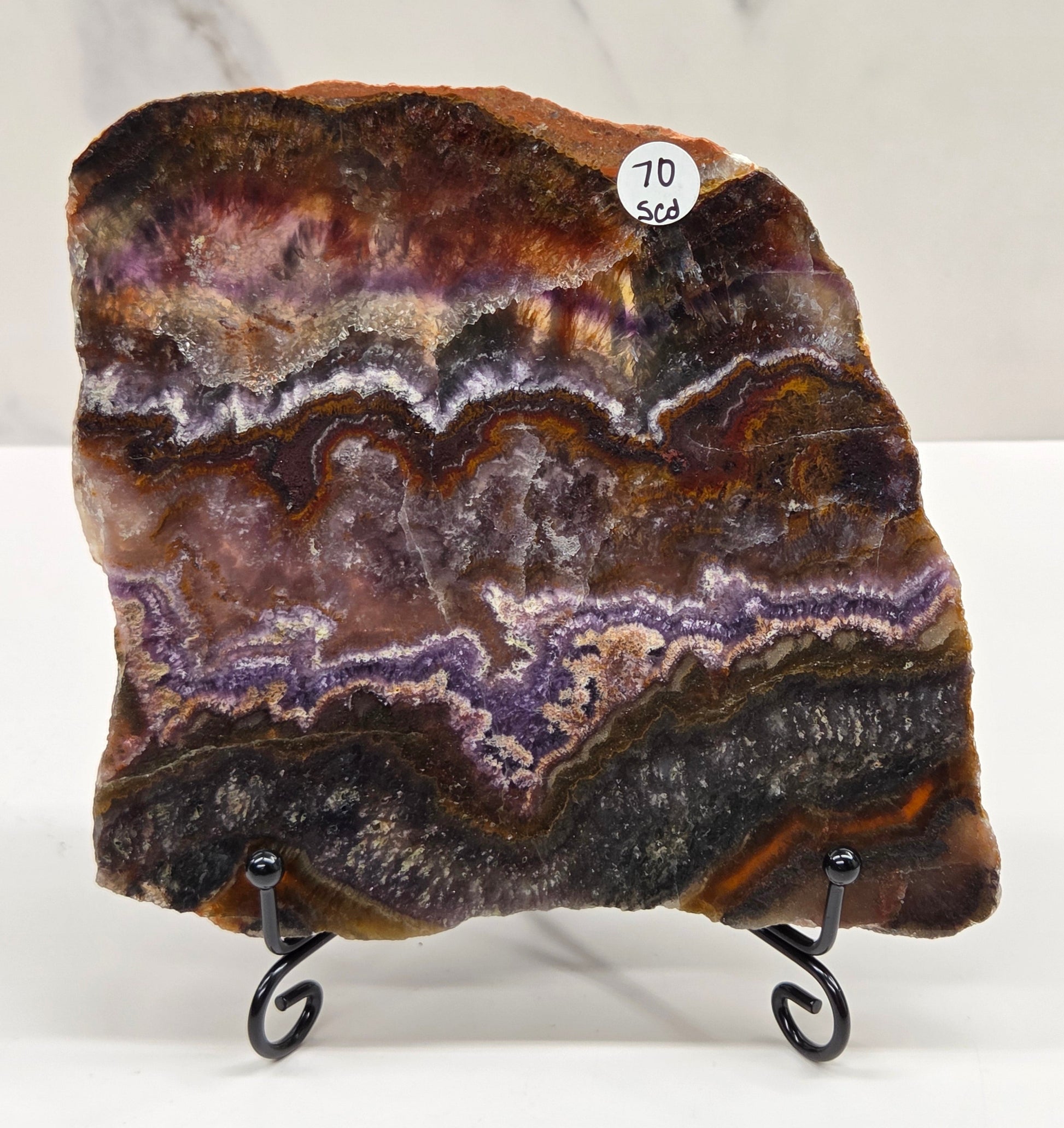Banded crystal slice with multiple colors and inclusions on a stand against a marble background