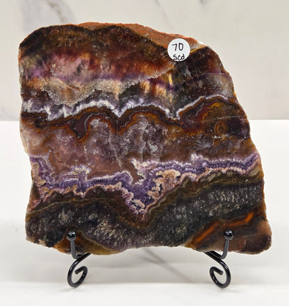 Banded crystal slice with multiple colors and inclusions on a stand against a marble background