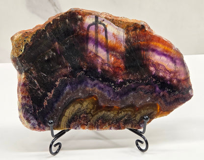 Banded crystal slice with multiple colors and inclusions on a stand against a marble background