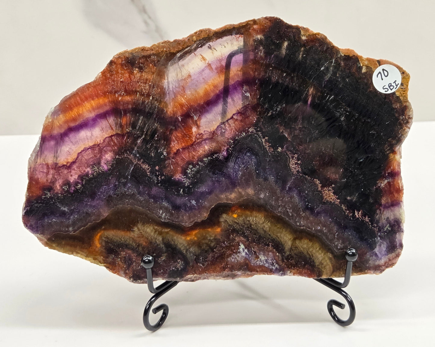 Banded crystal slice with multiple colors and inclusions on a stand against a marble background