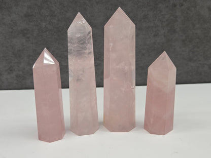 Four rose quartz crystal points of varying sizes on a white surface with a gray background