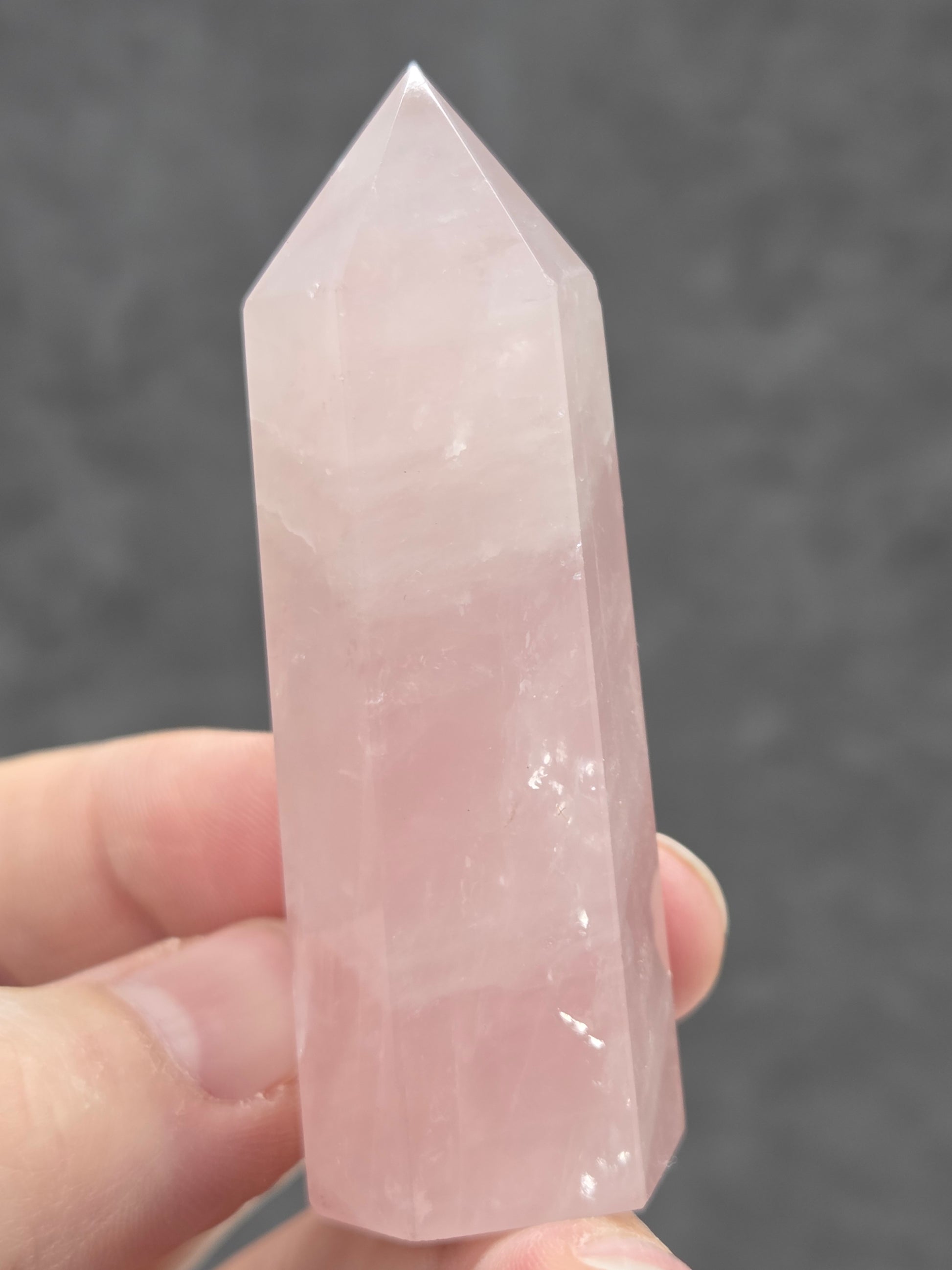 Hand holding a pink rose quartz crystal against a dark background