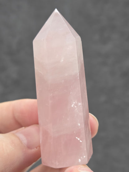 Hand holding a pink rose quartz crystal against a dark background